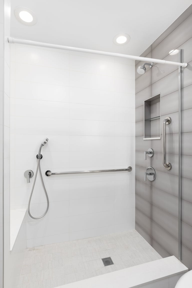 A walk-in shower with white and brown tiled walls, chrome faucet, bench seat, and a square tiled floor