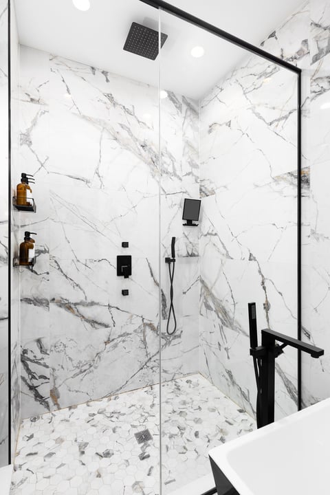 Luxury walk-in shower with marble tile walls, hexagon tile flooring, black shower fixtures and clear glass walls