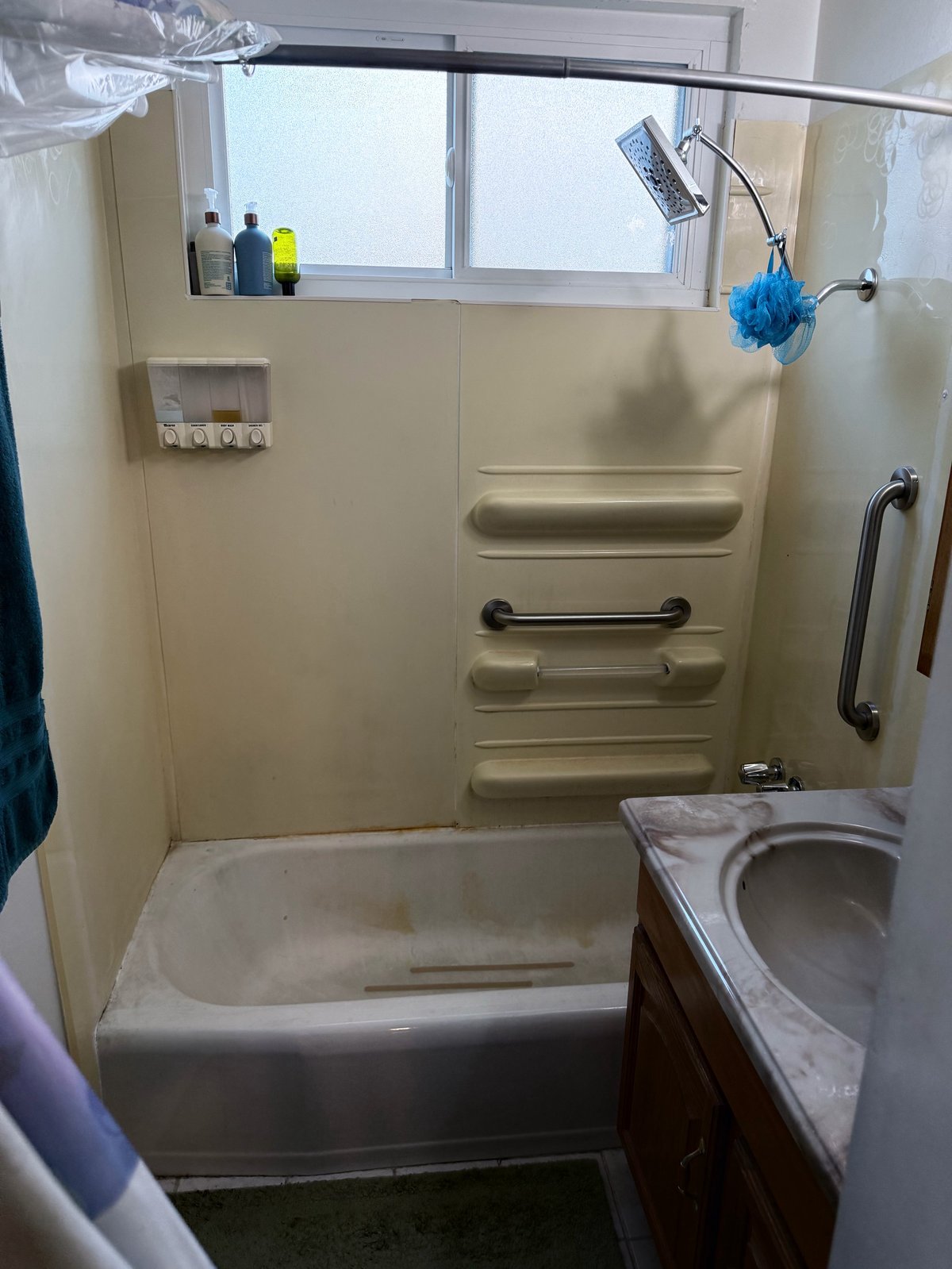 Bathroom with vintage cream-colored surround, white bathtub, wall-mounted shelving with toiletries, and window with natural light