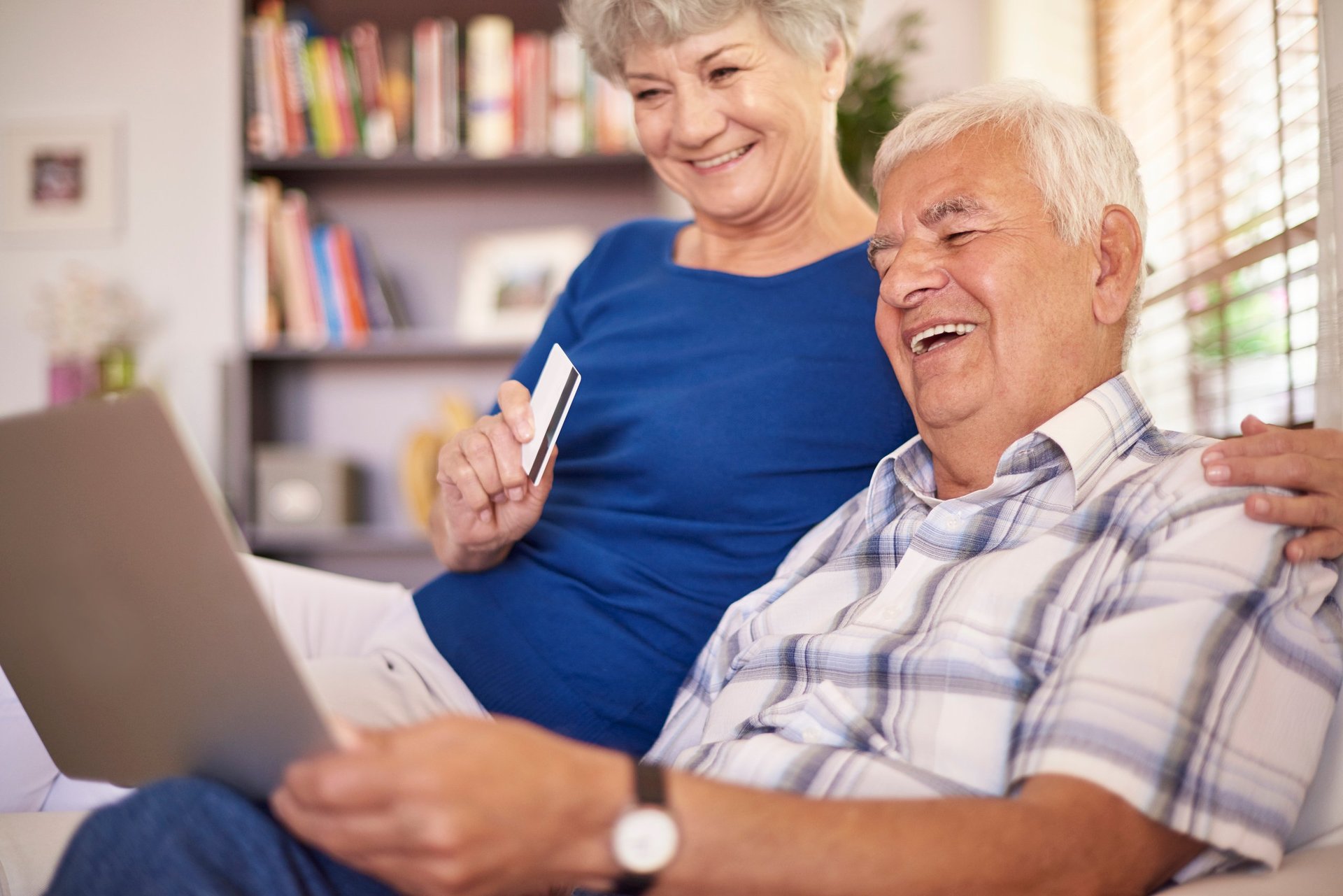 Senior couple smiling while using a laptop together in a home library setting