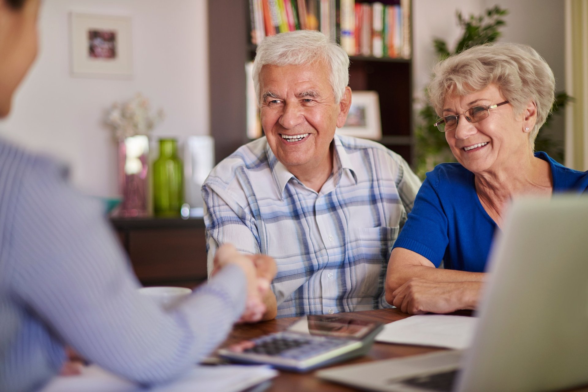 Elderly couple smiling while meeting with an advisor at a table with a laptop and documents in a home office setting