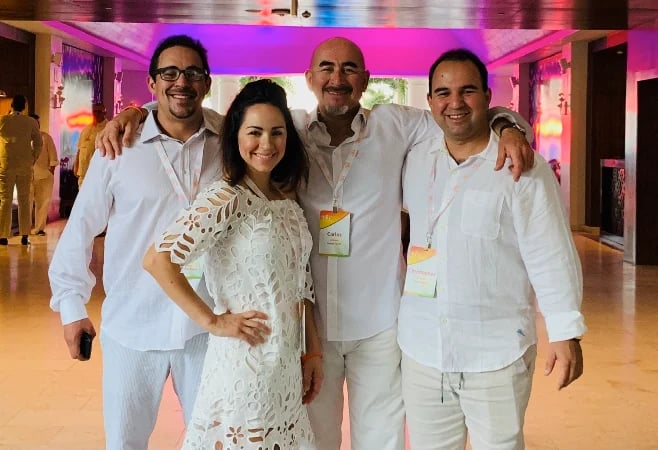 Four people in white clothing posing together at an indoor event with pink lighting in the background