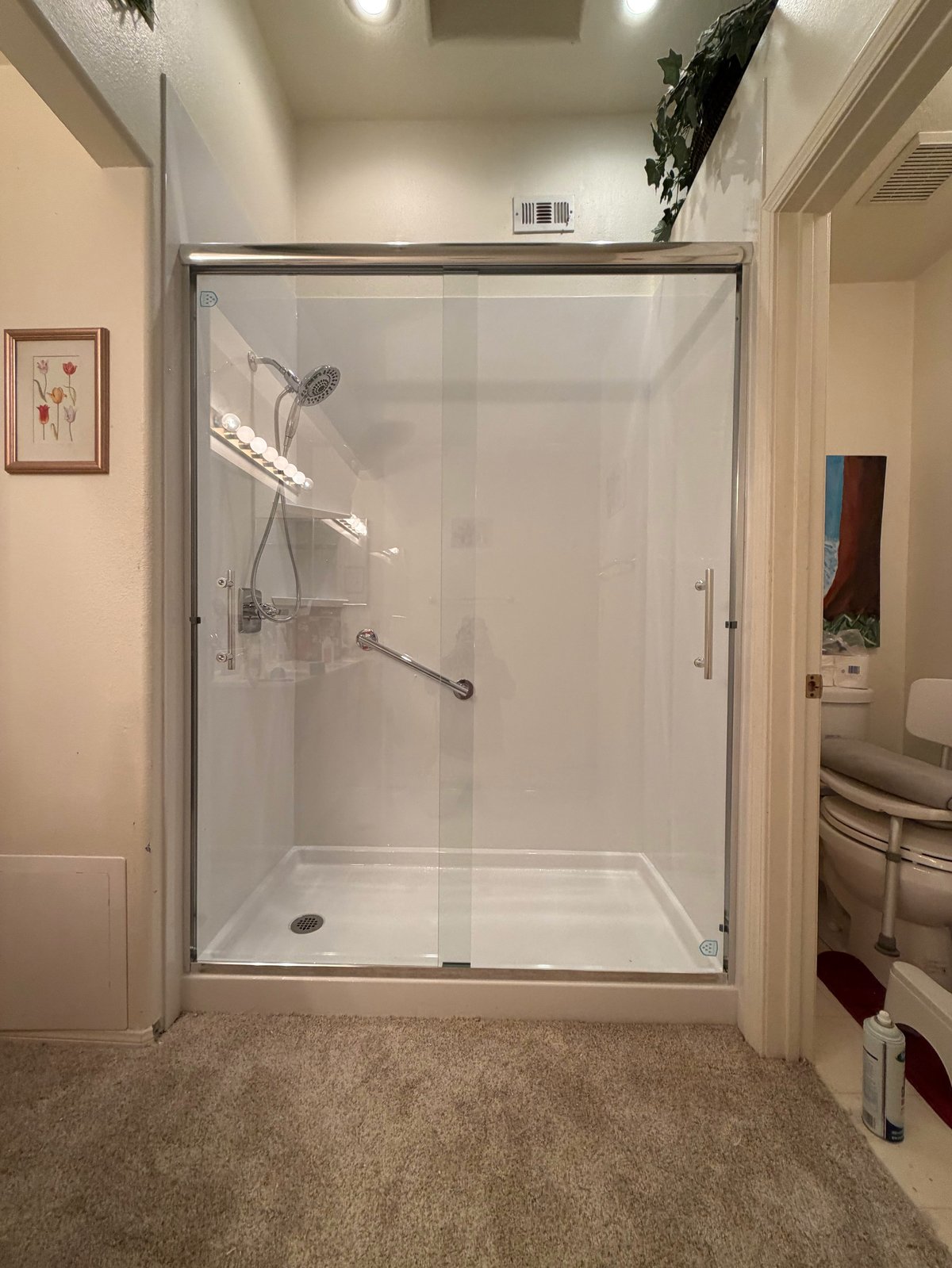 Modern bathroom with glass shower enclosure, white tile walls, toilet, and towels on mat in foreground